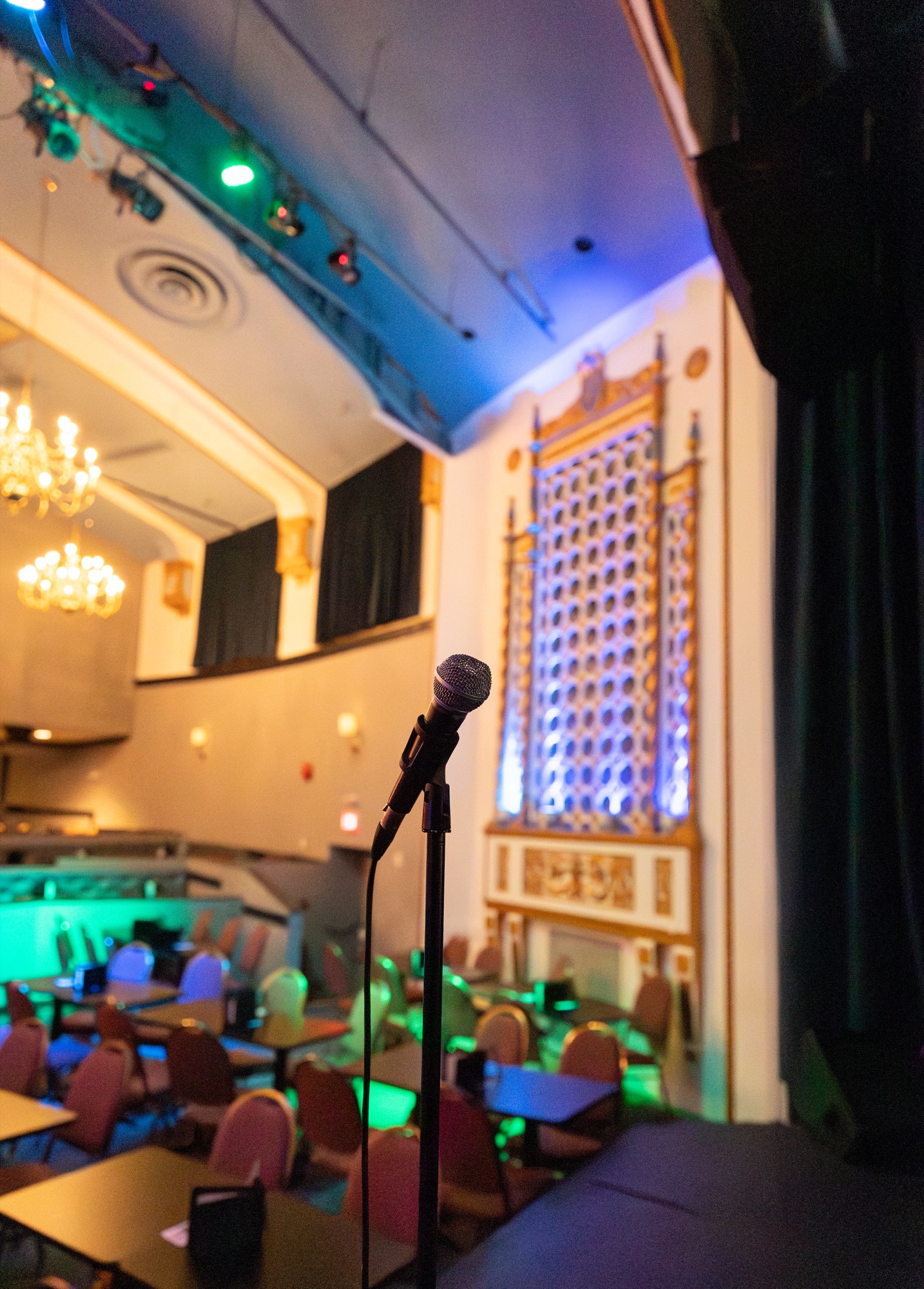 A microphone on stage at House of Comedy, beneath a chandelier and the Columbia Theatre's ornate lit panels