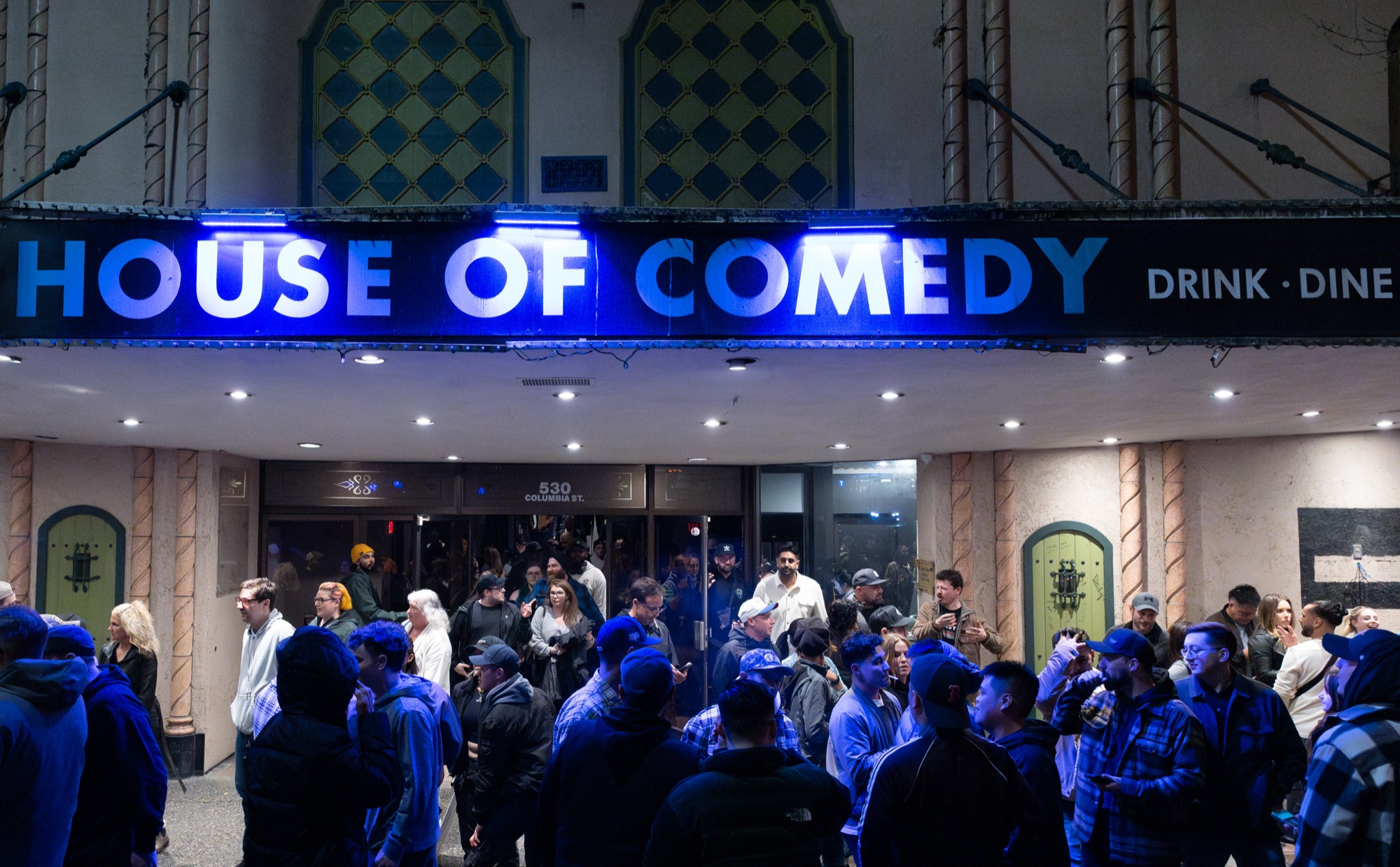 The lit House of Comedy marquee above the Columbia Theatre entrance, with a queue outside